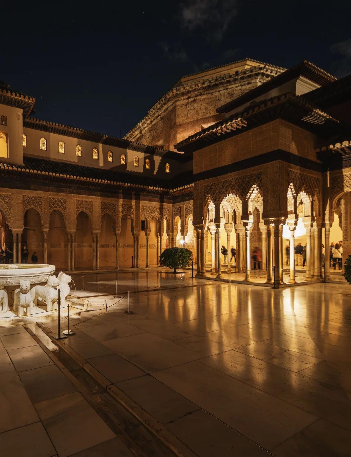 The Alhambra's Court of the Lions lit up at night, horseshoe arches reflected in the marble floor